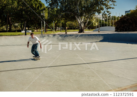Excited young man riding skateboard in skate park on sunny day. Extreme sport concept 112372591