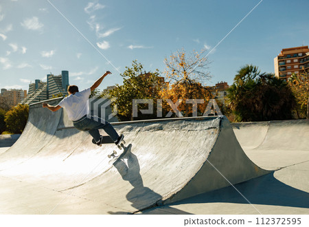Active skateboarder jumping and performing a trick in a ramp of a skate park 112372595
