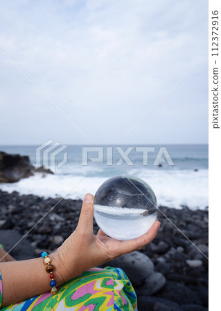woman meditating on beach shore and holding crystal ball 112372916