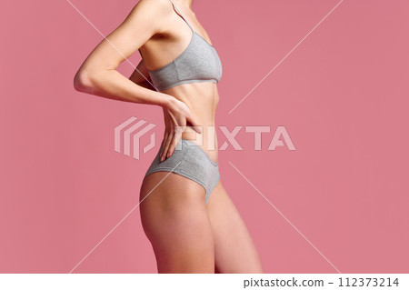 Side view of beautiful, fit woman in gray cotton underwear, showing slim waistline against pink studio background. Side view of beautiful, fit woman in gray cotton underwear, showing slim waistline against pink studio background. 112373214