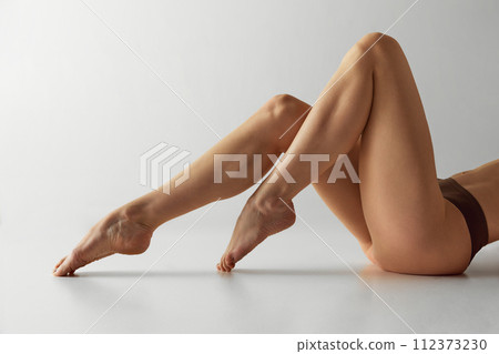 Close-up of a woman's toned, smooth legs against grey studio background. Muscular definition and active lifestyle. Waxing Close-up of a woman's toned, smooth legs against grey studio background. Muscular definition and active lifestyle. Waxing 112373230