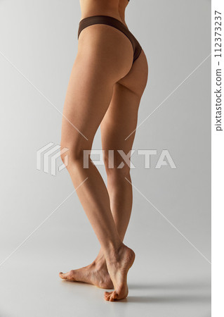 Smooth and toned legs. Cropped photo of young female legs, buttocks against grey studio background. Model in underwear. Smooth and toned legs. Cropped photo of young female legs, buttocks against grey studio background. Model in underwear. 112373237
