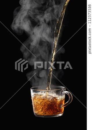 Process brewing tea on black background. Transparent glass cup of freshly brewed black tea steaming isolated 112373586