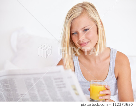 Young woman, smile and orange juice with newspaper on bed, headlines and drink for health body in wellness. Blonde model, thirsty or glass of fruit cocktail to detox, morning or vitamin c in bedroom Young woman, smile and orange juice with newspaper on bed, headlines and drink for health body in wellness. Blonde model, thirsty or glass of fruit cocktail to detox, morning or vitamin c in bedroom 112373680