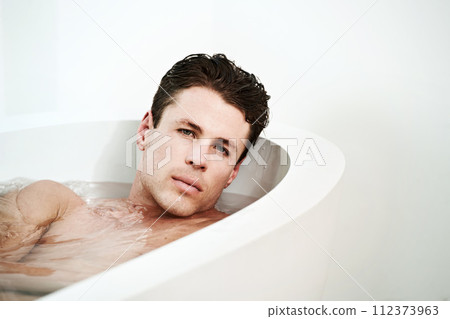 Man, bathtub and portrait for relax in bathroom with serious face, wellness and confidence in the morning. Model, person and lying down in bath for self care, grooming and cosmetic routine or topless Man, bathtub and portrait for relax in bathroom with serious face, wellness and confidence in the morning. Model, person and lying down in bath for self care, grooming and cosmetic routine or topless 112373963