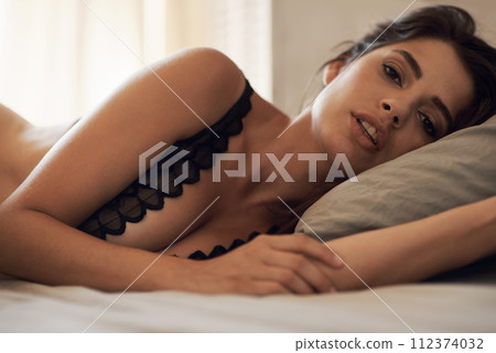 Serious, portrait and woman relaxing in bed for rest, break or sleeping at modern apartment. Beautiful, confident and young female person from Mexico laying on pillow in bedroom with lingerie at home 112374032