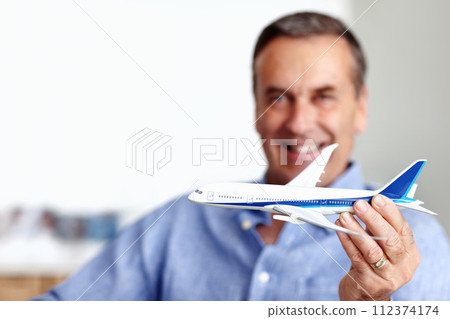 Mature man, flight and toy plane for travel, vacation and holiday planning with a smile at home. Happy, airplane model and retirement of a male person with confidence from trip and air traveling Mature man, flight and toy plane for travel, vacation and holiday planning with a smile at home. Happy, airplane model and retirement of a male person with confidence from trip and air traveling 112374174