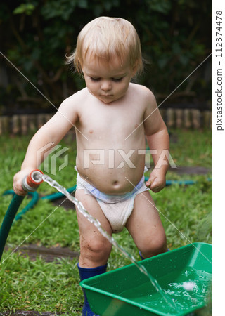 Baby, playing with hose and gardening, water and development with bucket, curiosity and backyard. Toddler, child and infant in garden, alone and childhood for skills, milestone and coordination Baby, playing with hose and gardening, water and development with bucket, curiosity and backyard. Toddler, child and infant in garden, alone and childhood for skills, milestone and coordination 112374478