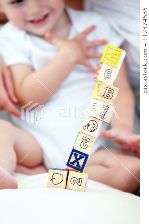 Baby, kid and playing with blocks for learning, smile and happy in home nursery on bed. Toddler, wood and child with toys for alphabet, education and development of cute boy with numbers closeup 112374535