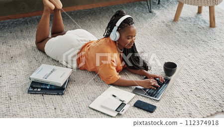 Laptop, headphones and young woman on the floor in living room of modern apartment. Tech, smile and young African female university student study and listen to music on computer in lounge at home. 112374918