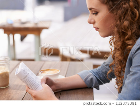 Reading, coffee and woman with book in restaurant in morning with literature novel for knowledge. Diner, calm and young female person enjoying story and drinking cappuccino, latte or espresso in cafe 112375381