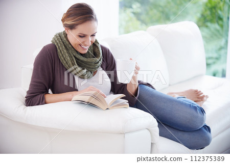 Happy woman, book and reading with coffee on sofa for story, novel or knowledge in living room at home. Lady, fiction books and drinking cup of tea for literature, hobby or comfortable break on couch Happy woman, book and reading with coffee on sofa for story, novel or knowledge in living room at home. Lady, fiction books and drinking cup of tea for literature, hobby or comfortable break on couch 112375389