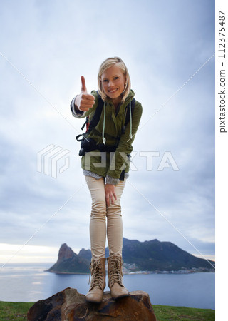 Woman, hiking and thumbs up on mountain for fitness, outdoor and travel with success, vote and goals in Europe. Portrait of person in backpack and like or yes hand for trekking or adventure by island 112375487
