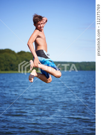 Portrait, jump and ocean with water, vacation and excited with happiness, weekend break and movement. Person, outdoor and guy with water, cheerful and extreme with nature, seaside and energetic 112375769