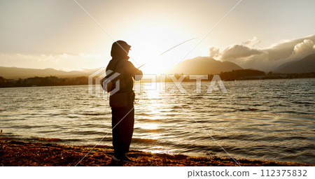 Person, fishing and water in morning, sunrise and sport by ocean, lake and river with equipment in nature. Fisherman, line and catch fish for games, food and silhouette in sunshine, dawn and horizon 112375832