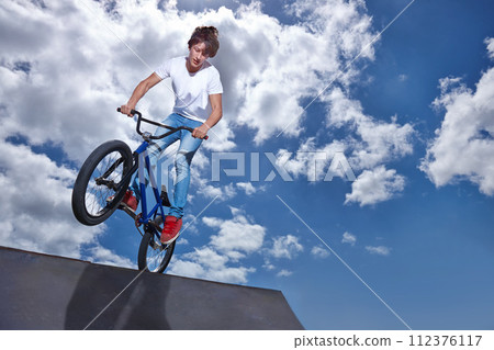Riding, bike and teen on ramp for sport performance, jump or training for event at park with blue sky mockup. Bicycle, stunt or kid balance on edge of board in trick for cycling competition challenge 112376117