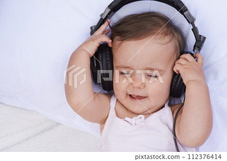 Baby, headphones and streaming music to relax, radio and listening to podcast on bed at home. Girl, kid and hearing sound for child development or learning, toddler and calming playlist for audio Baby, headphones and streaming music to relax, radio and listening to podcast on bed at home. Girl, kid and hearing sound for child development or learning, toddler and calming playlist for audio 112376414