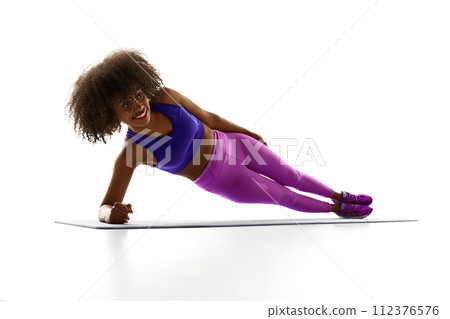 Strength and power. Young, focused African-American woman stands in side-plank against white studio background. Abdominal exercises. Strength and power. Young, focused African-American woman stands in side-plank against white studio background. Abdominal exercises. 112376576