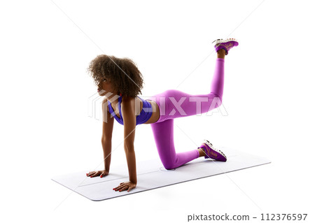 Young African-American woman training leg muscles, buttocks against white studio background. Perfect body shapes. 112376597