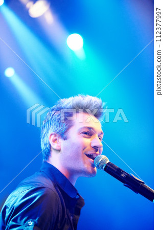 Man, singing and performing at night, music festival and stage for concert, party and entertaining crowd. Microphone, musician and rave on weekend, event and rockstar in club for celebration Man, singing and performing at night, music festival and stage for concert, party and entertaining crowd. Microphone, musician and rave on weekend, event and rockstar in club for celebration 112377997