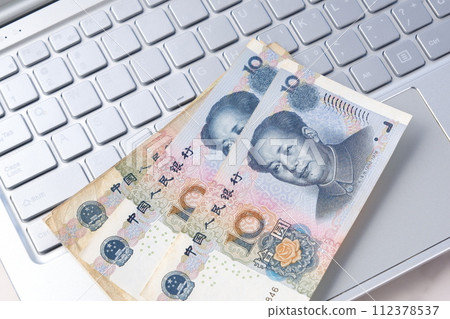 Chinese currency, Renminbi (RMB) banknotes and a laptop with a portrait of Mao Zedong Chinese currency, Renminbi (RMB) banknotes and a laptop with a portrait of Mao Zedong 112378537