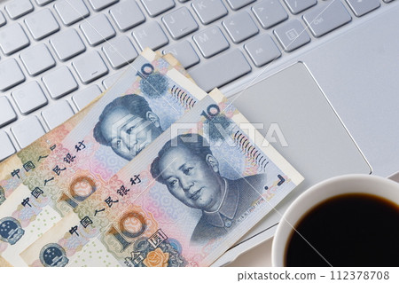Chinese currency, Renminbi (RMB) banknotes with a portrait of Mao Zedong, a laptop and a coffee cup with coffee Chinese currency, Renminbi (RMB) banknotes with a portrait of Mao Zedong, a laptop and a coffee cup with coffee 112378708