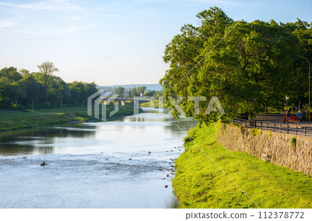 river uzh at sunrise. trees on the grassy embankment in morning light. bridge in the distance 112378772
