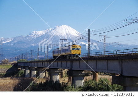 Rear view of a local train (2-car train) passing the Hino River railway bridge with Mt. Daisen in the background 112379313