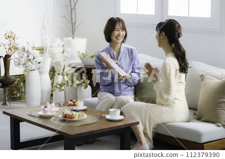 Mother's Day: A daughter in her 30s giving a gift and her mother receiving it in a hotel tea room Mother's Day: A daughter in her 30s giving a gift and her mother receiving it in a hotel tea room 112379390