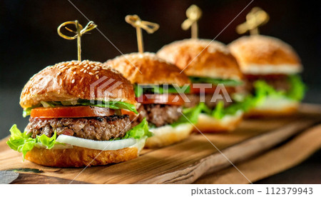 Many mini hamburgers lined up on a wooden board Many mini hamburgers lined up on a wooden board 112379943