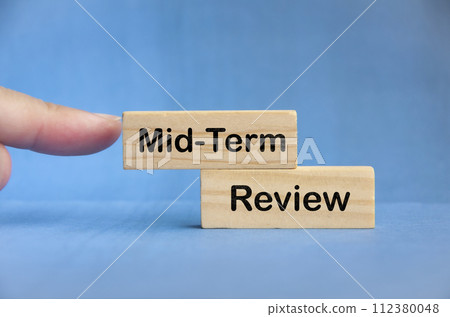 Finger pointing Mid Term Review text on wooden block with blue background. Mid Term budgeting concept. Finger pointing Mid Term Review text on wooden block with blue background. Mid Term budgeting concept. 112380048