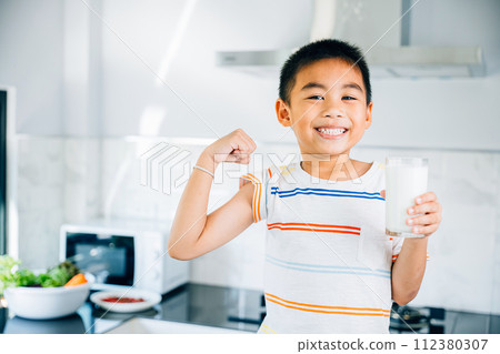 Cheerful Asian little boy holds milk in kitchen, smiling brightly. Portrait of cute son enjoying drink. Joyful child sips calcium-rich liquid, radiating happiness at home give me. Cheerful Asian little boy holds milk in kitchen, smiling brightly. Portrait of cute son enjoying drink. Joyful child sips calcium-rich liquid, radiating happiness at home give me. 112380307