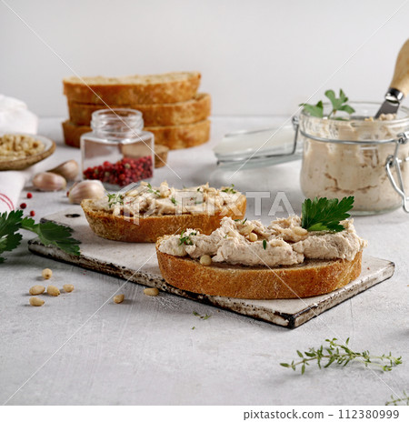 Homemade pate, spread or mousse in glass jar with sliced bread and herbs, light concrete background. 112380999
