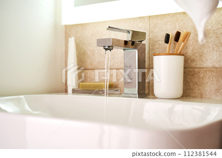 Bathroom sink with toothbrushes and running water. 112381544