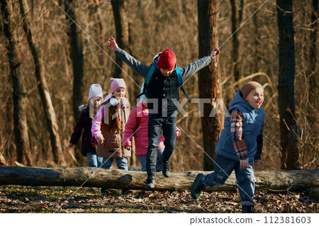 Candid moment of children, classmates in hats and jackets on sunny, brisk walk and enjoying nature. Outdoor activities for children's development. Candid moment of children, classmates in hats and jackets on sunny, brisk walk and enjoying nature. Outdoor activities for children's development. 112381603