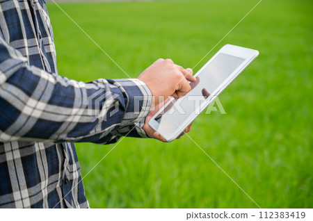 Close up of a Farmer man read or analysis a report in tablet computer on a green agriculture field.  112383419