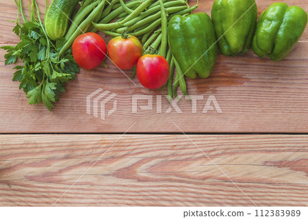 Frame of red tomatoes, green bell peppers, cucumber, green beans and parsley on a wooden background Frame of red tomatoes, green bell peppers, cucumber, green beans and parsley on a wooden background 112383989