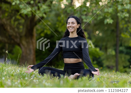 Content young female in activewear enjoys yoga meditation in peaceful park, embodying wellness and mindfulness. 112384227