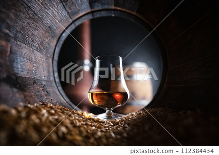 A glass of bourbon Whiskey in oak barrel 112384434
