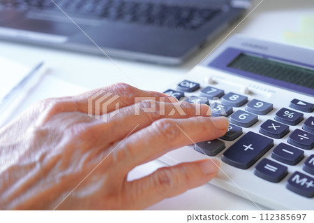Close-up of senior woman's hand checking pension amount on calculator Close-up of senior woman's hand checking pension amount on calculator 112385697