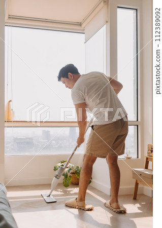 Asian Thai man using mop for cleaning floor in living room apartment, Man do household chores, housework concept. 112389092