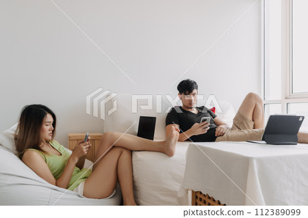 Asian Thai couple using laptop, Both man and woman busy working on notebook, lover freelancer sitting on couch in room apartment. Asian Thai couple using laptop, Both man and woman busy working on notebook, lover freelancer sitting on couch in room apartment. 112389099