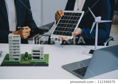 Two Young Engineers Expertise in Solar Cell Installation Meetings and Discussion in The Job. Planning to Install Solar Photovoltaic Panels on Roof Top in The Office Room with Factory Building Plan. 112390870