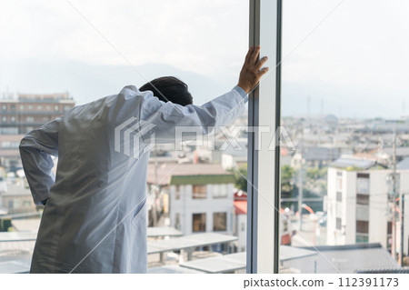 Male doctor leaning against the glass window (stress, overwork, fatigue, worried, thinking) 112391173