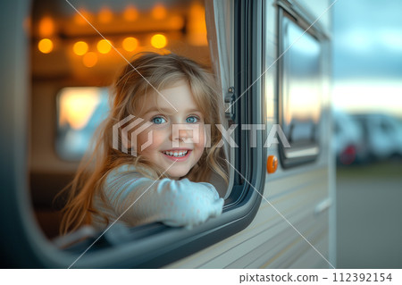 A cheerful girl looks out of the window of a motorhome 112392154
