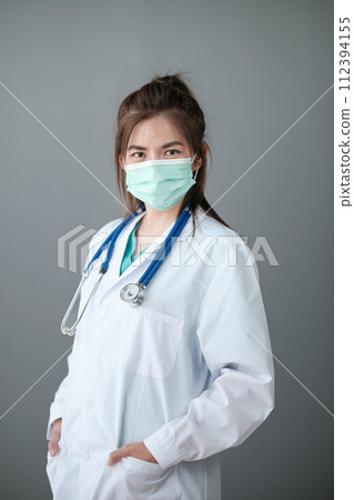 Young Asian female doctor standing on grey background. Young Asian female doctor standing on grey background. 112394155