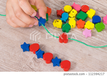 Preschooler making bracelet from thread and colored beads. Development of kids motor skills 112394217