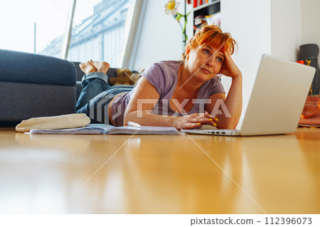 portrait woman lying on parquet floor with laptop, notebooks, emotions on face 112396073