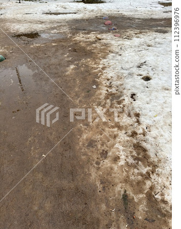 Melting dirty snow on the streets of the city during the daytime in winter. Snow with sand and mud lies on the road Melting dirty snow on the streets of the city during the daytime in winter. Snow with sand and mud lies on the road 112396976