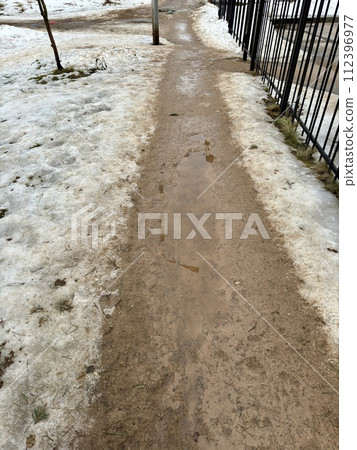 Melting dirty snow on the streets of the city during the daytime in winter. The pedestrian road is snow with sand and mud. Traces of people and pets Melting dirty snow on the streets of the city during the daytime in winter. The pedestrian road is snow with sand and mud. Traces of people and pets 112396977